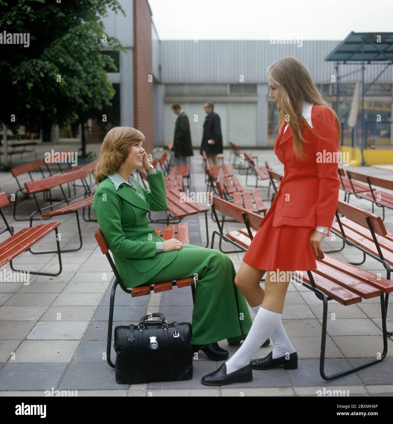 In the 1970s. Two young women dressed in typical 1970s fashion and colors. One girl dressed in a red dress with white socks. One in a matching green jacket and wide legged trousers that were in fashion then.  Sweden june 19 1972. Stock Photo