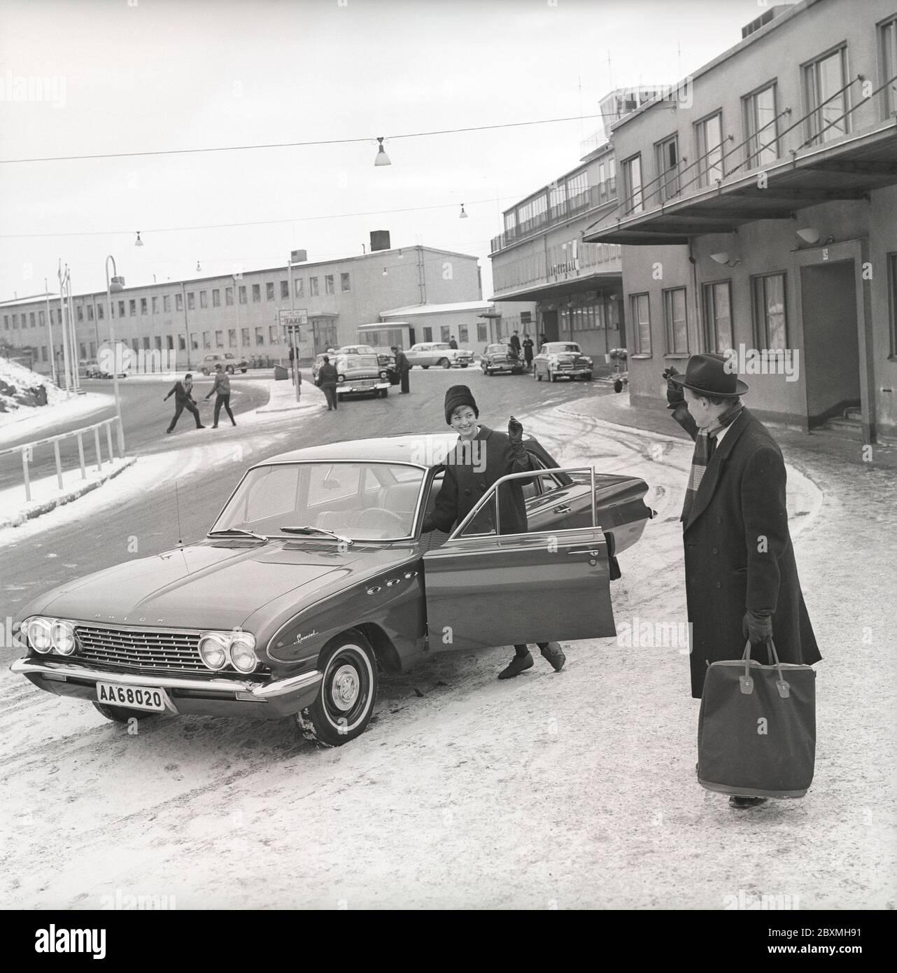 Couple in the 1960s. A woman has driven her husband to the airport and waves at him from her car, a Buick Special model 1961. It's a winter day at Bromma airport in Stockholm. Sweden 1961. Kristoffersson ref CS5-4 Stock Photo