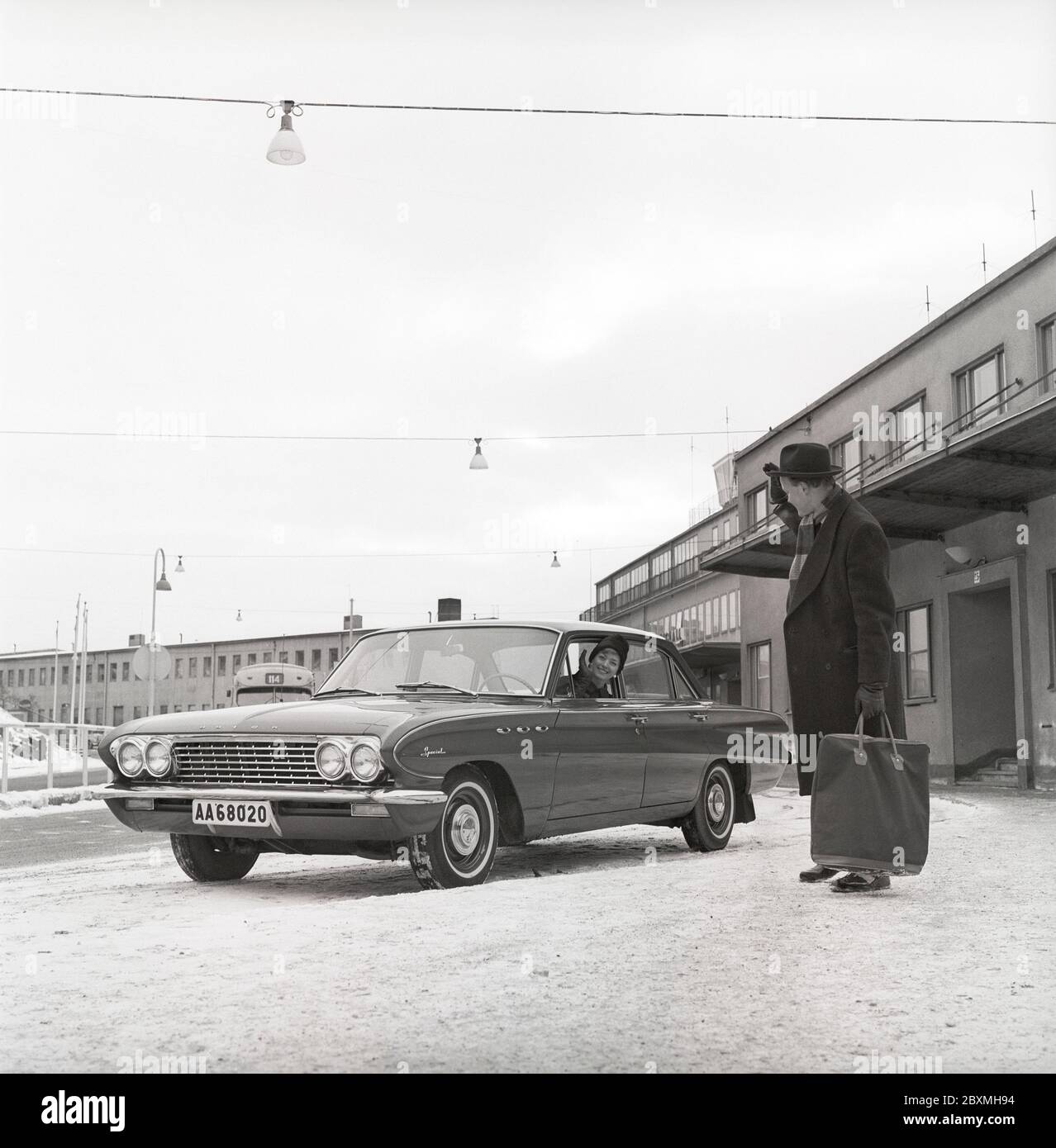 Couple in the 1960s. A woman has driven her husband to the airport and waves at him from her car, a Buick Special model 1961. It's a winter day at Bromma airport in Stockholm. Sweden 1961. Kristoffersson ref CS5-8 Stock Photo