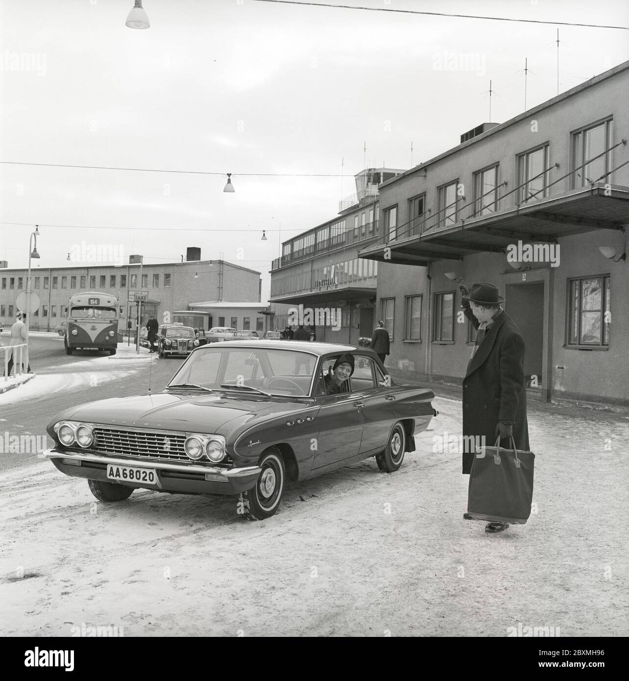 Couple in the 1960s. A woman has driven her husband to the airport and waves at him from her car, a Buick Special model 1961. It's a winter day at Bromma airport in Stockholm. Sweden 1961. Kristoffersson ref CS5-10 Stock Photo