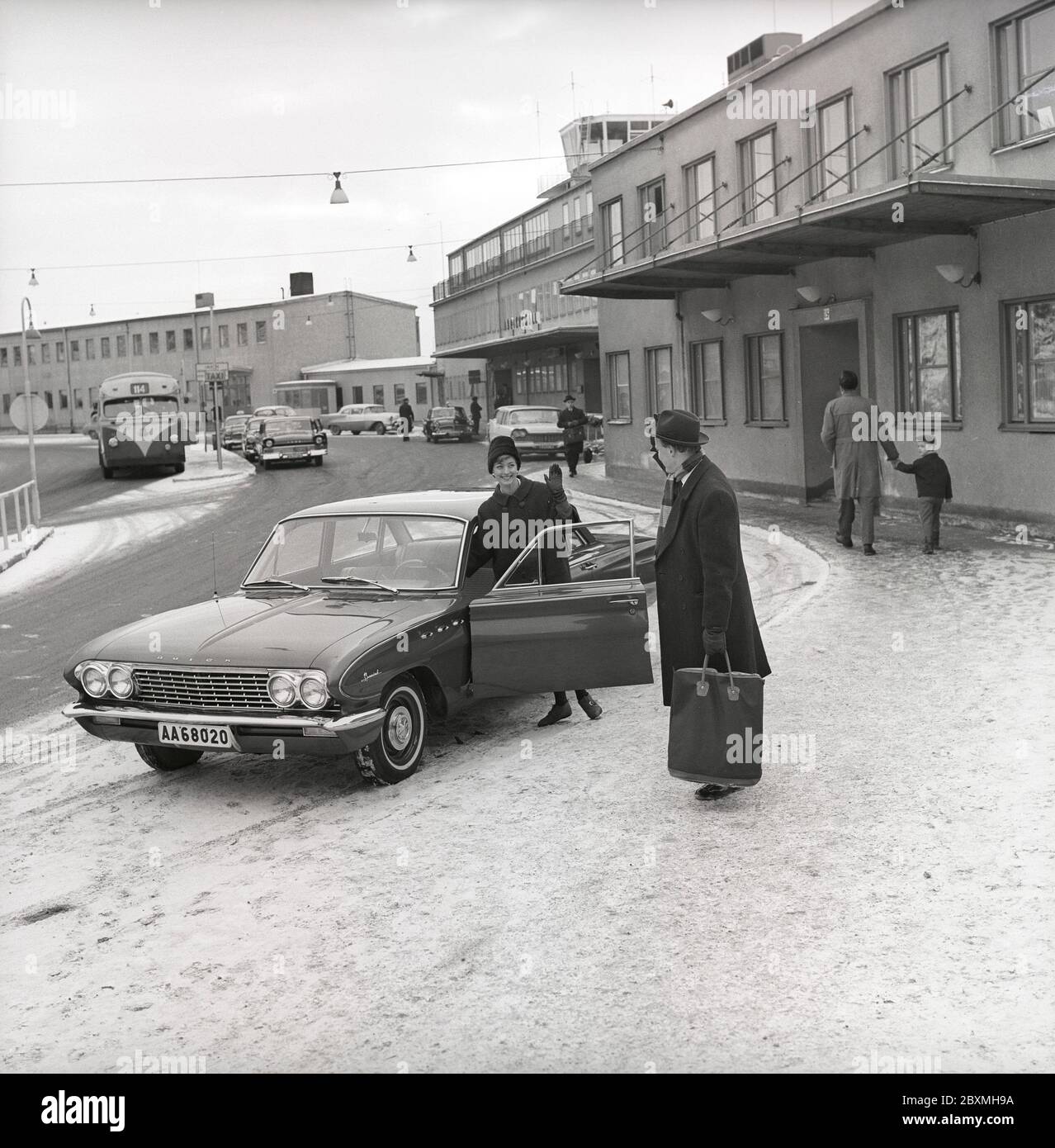 Couple in the 1960s. A woman has driven her husband to the airport and waves at him from her car, a Buick Special model 1961. It's a winter day at Bromma airport in Stockholm. Sweden 1961. Kristoffersson ref CS5-1 Stock Photo