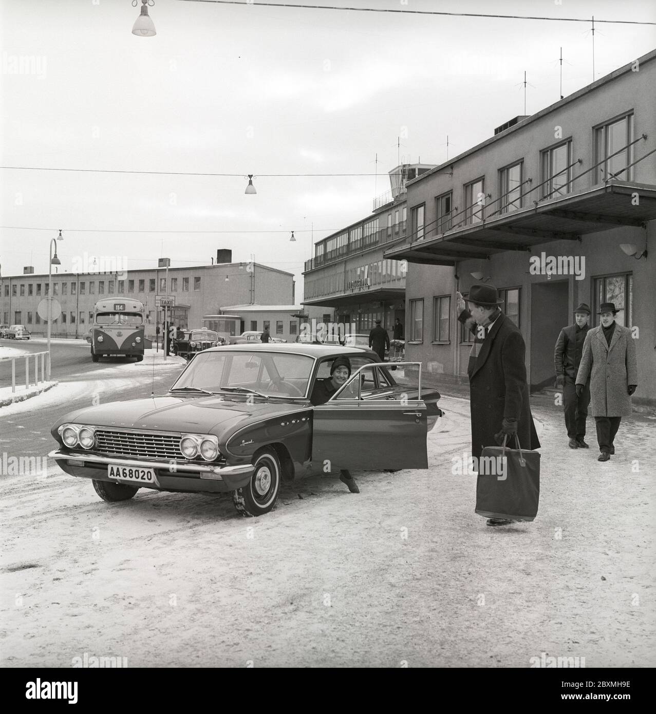 Couple in the 1960s. A woman has driven her husband to the airport and waves at him from her car, a Buick Special model 1961. It's a winter day at Bromma airport in Stockholm. Sweden 1961. Kristoffersson ref CS5-10 Stock Photo