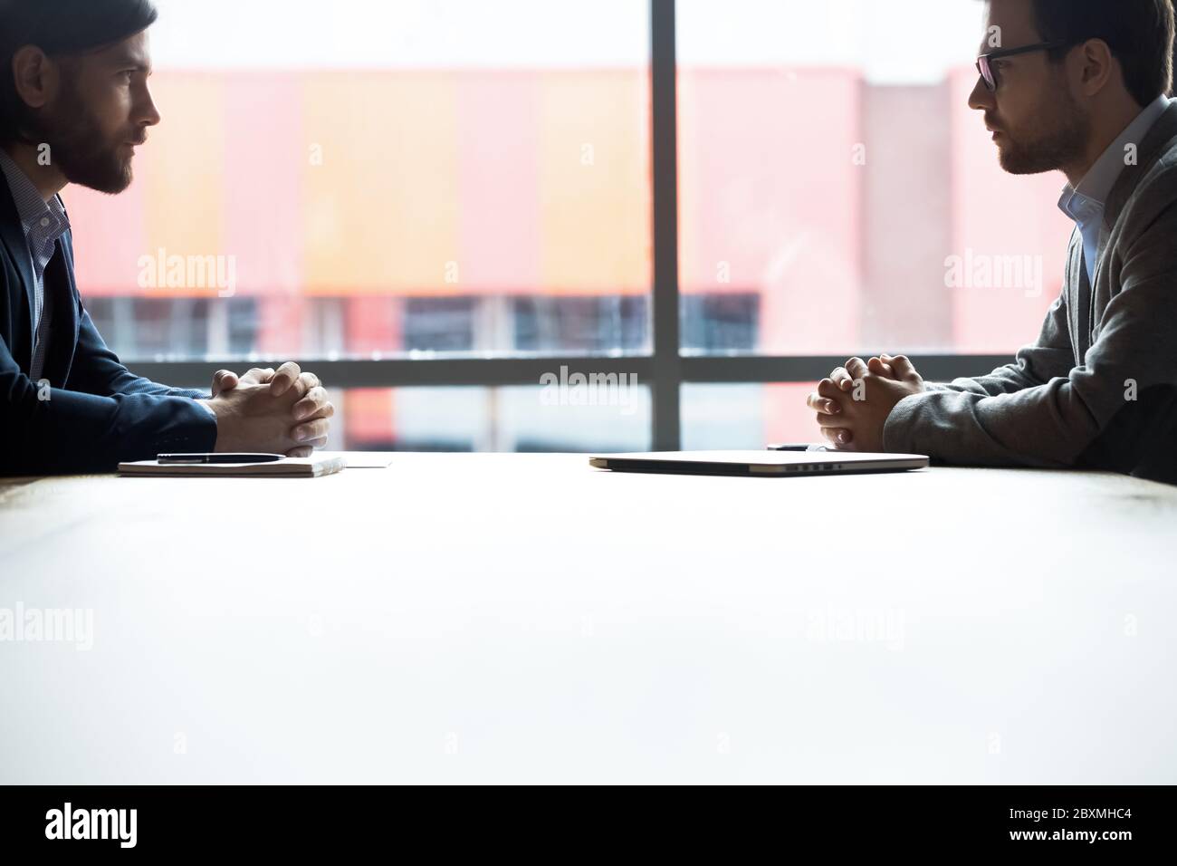 Two serious businessmen sitting at desk looking at each other Stock Photo