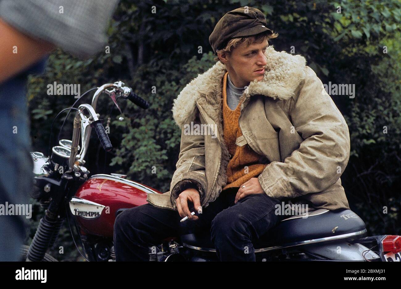 In the 1960s. A young man on his Triumph motorcycle. The law of wearing a safety helmet is not yet in force and at this time it was popular to wear caps. The jacket is typical 1960s with a wool collar. Sweden 1968 Stock Photo