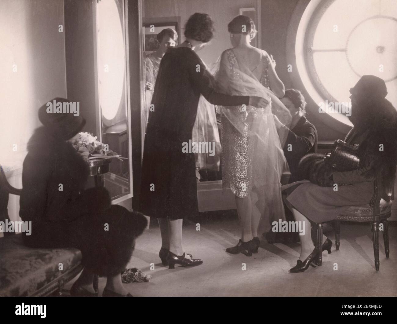 Back in the 1920s. At the department store NK in Stockholm, a woman is standing in front of a mirror trying on a dress. Two women of the staff is adjusting details to make it fit perfectly. Perhaps a dress for a celebration or a party, it is the roaring twenties after all. Stock Photo