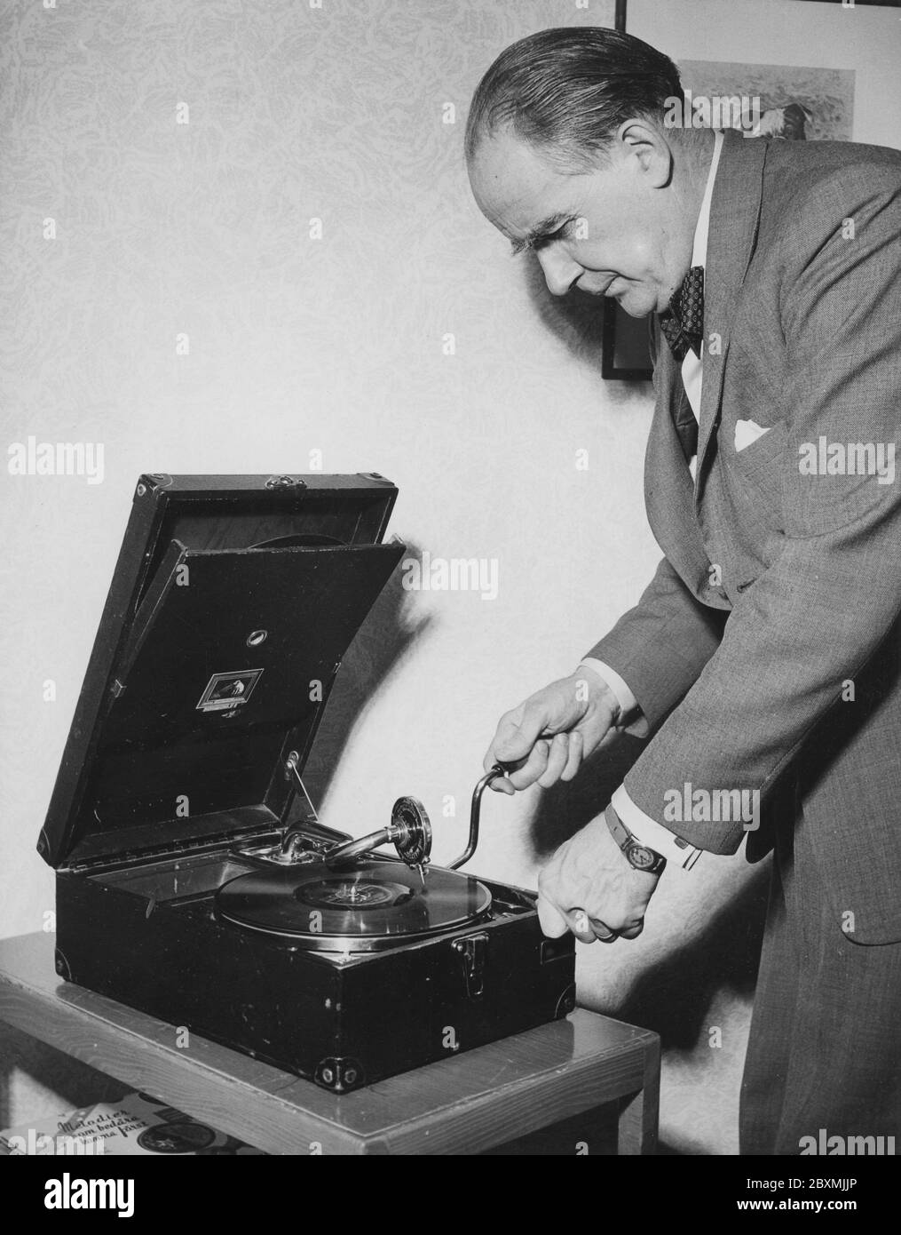 Hugo Lindh. 1899-1979. Swedish composer at home operating his portable gramophone player. It's operated by winding it up with a lever. The record then plays. When your hear that the recording begins to slow down, you know you have to wind i up again. The records were made of fragile material and the speed of the record to sound as it should was 78 revolutions per minute. Sweden 1940s. Stock Photo