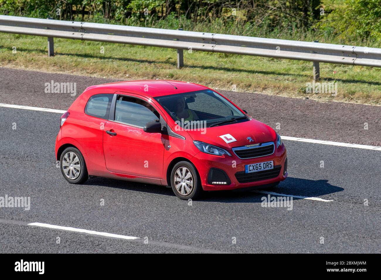 2015 red Peugeot 108 Access; Learner driver motorway training, under instruction, driving school, drivers, motorway driving lessons, approved driving instructor, supervised tution, instructor; Vehicular traffic L plates on moving vehicles, driving vehicle on UK roads, motors, motoring on the M6 motorway highway Stock Photo
