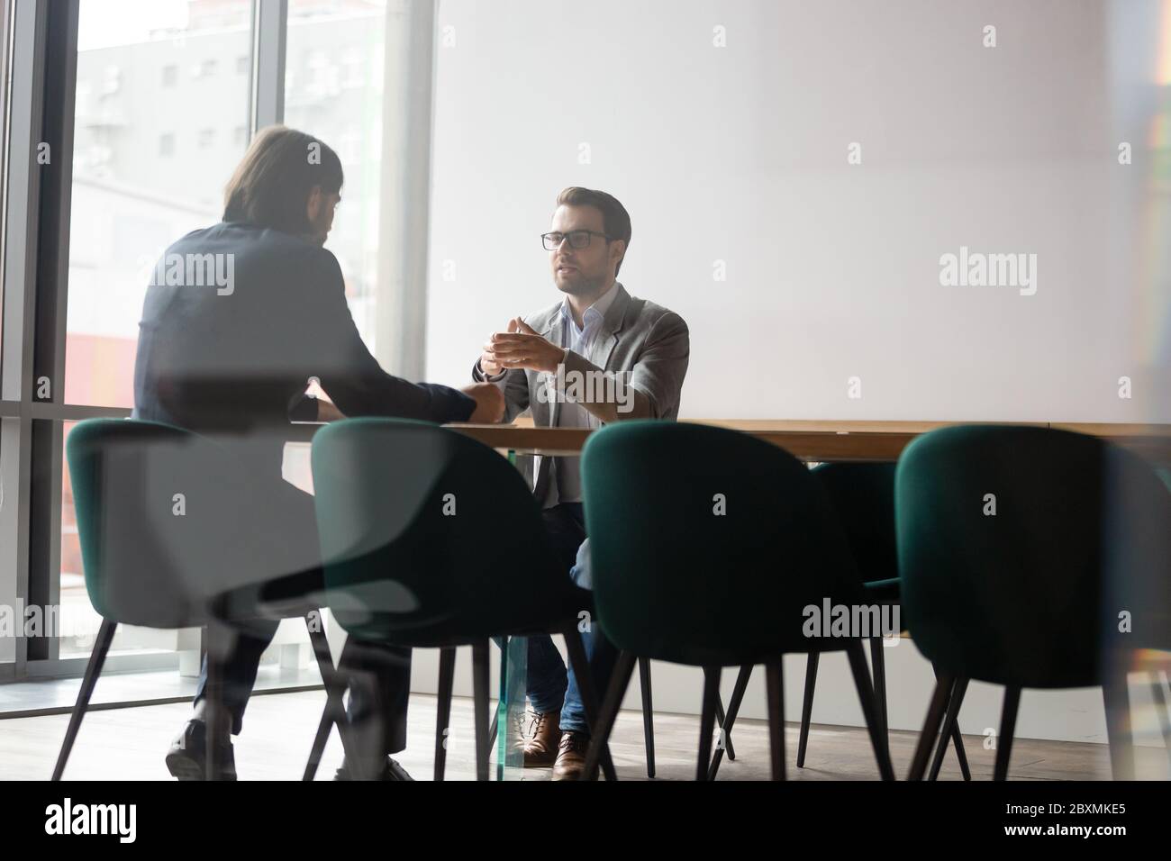 Behind glass wall two businessmen negotiating seated at boardroom desk Stock Photo