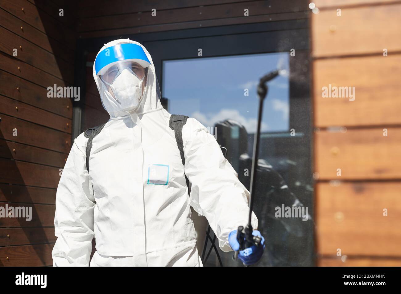 Waist up portrait of male worker wearing protective gear spraying chemicals to camera outdoors during disinfection, copy space Stock Photo