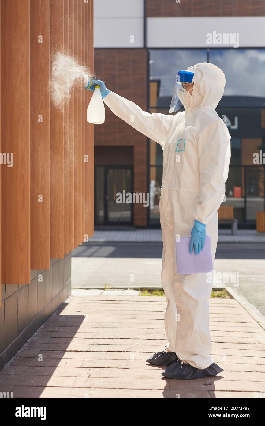 Side view full length portrait of one worker spraying chemicals over building outdoors during disinfection or cleaning Stock Photo