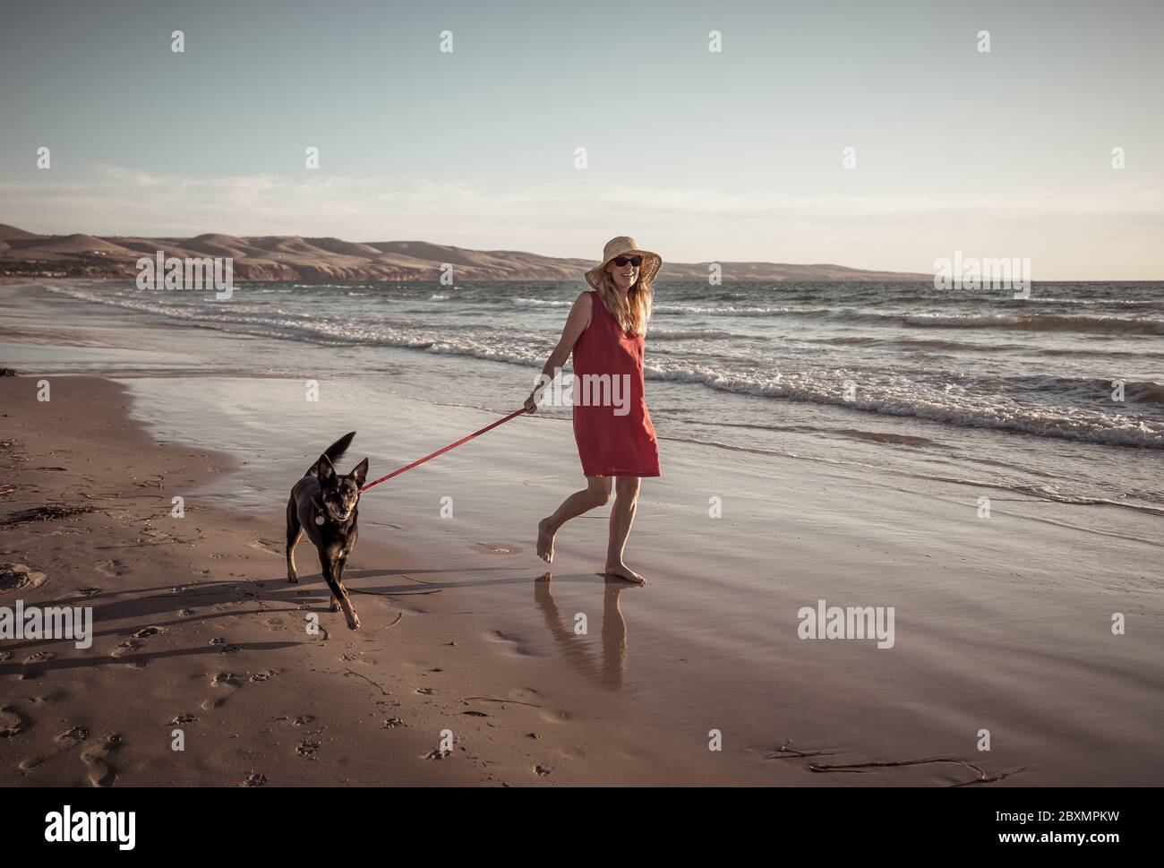 Beautiful mature retired woman and pet dog walking together on empty remote beach. In Outdoors exercise Hope and back to new normal life after Coronav Stock Photo