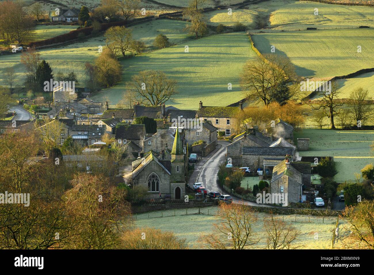 Burnsall (scenic Yorkshire Dales village) in valley, attractive cottages, country lane, green hillside fields (sunny winter morning) - England, GB, UK Stock Photo