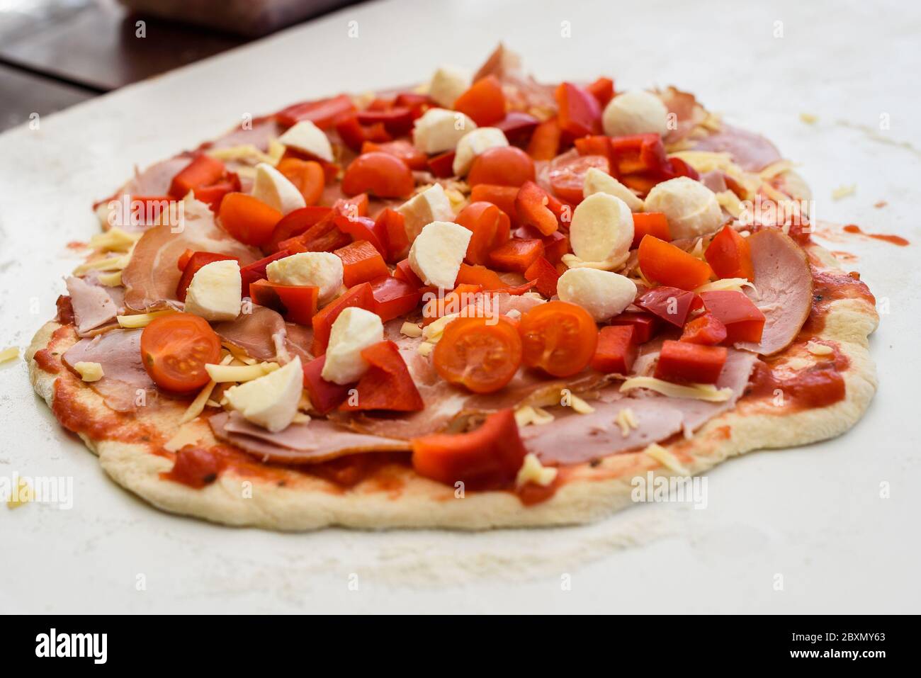 Making of homemade Italian pizza in fireplace brick oven. Making of pizza and adding different ingredients before baking it in outside fireplace. Raw Stock Photo