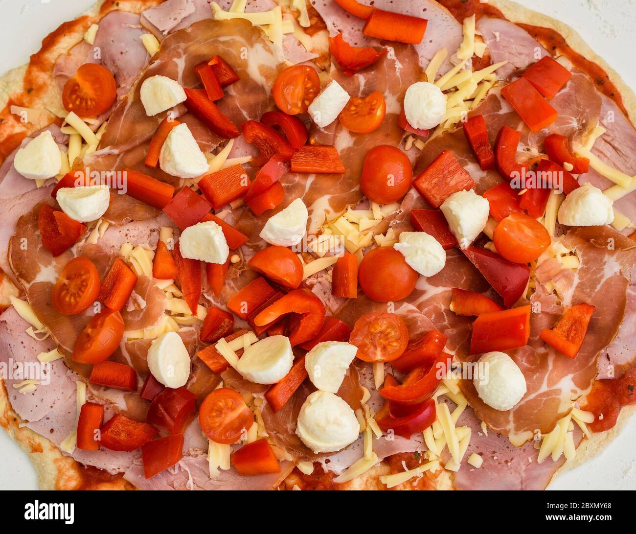 Making of homemade Italian pizza in fireplace brick oven. Making of pizza and adding different ingredients before baking it in outside fireplace. Raw Stock Photo