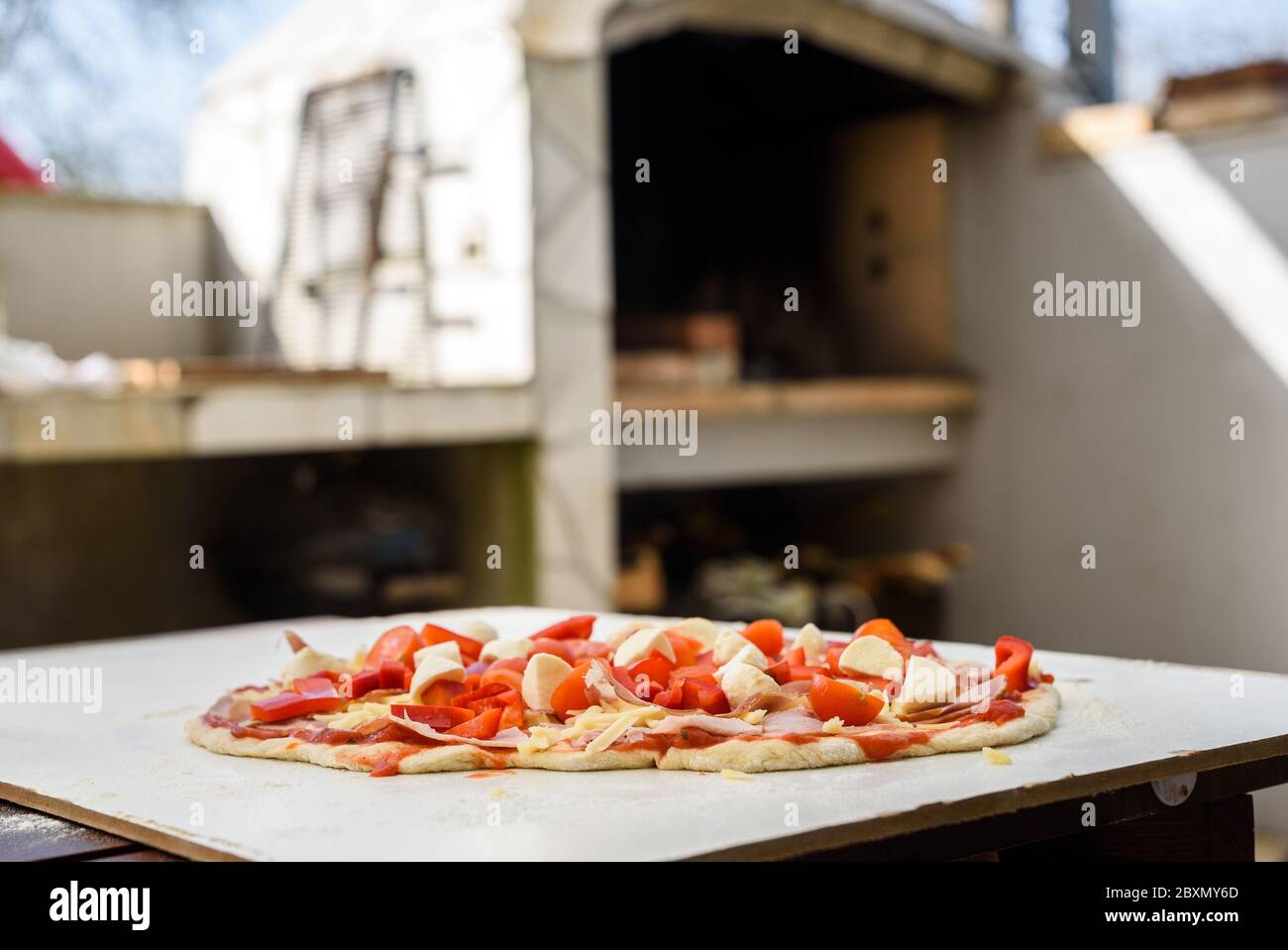 Making of homemade Italian pizza in fireplace brick oven. Making of pizza and adding different ingredients before baking it in outside fireplace. Raw Stock Photo