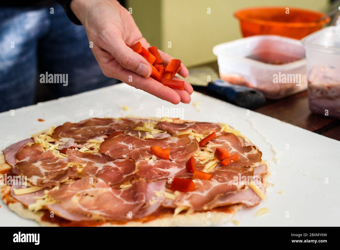 Making of homemade Italian pizza in fireplace brick oven. Making of pizza and adding different ingredients before baking it in outside fireplace. Hand Stock Photo