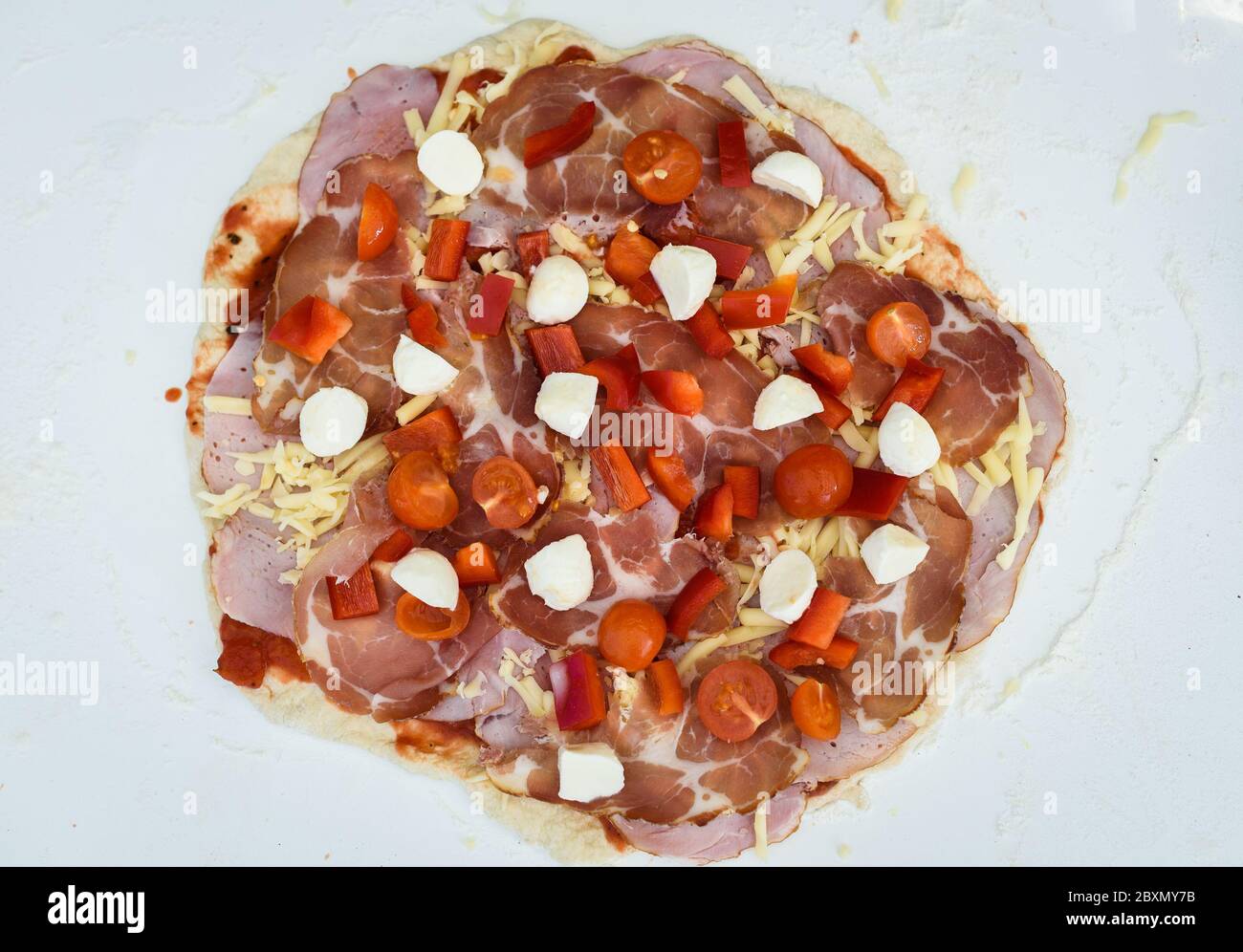 Making of homemade Italian pizza in fireplace brick oven. Making of pizza and adding different ingredients before baking it in outside fireplace. Raw Stock Photo