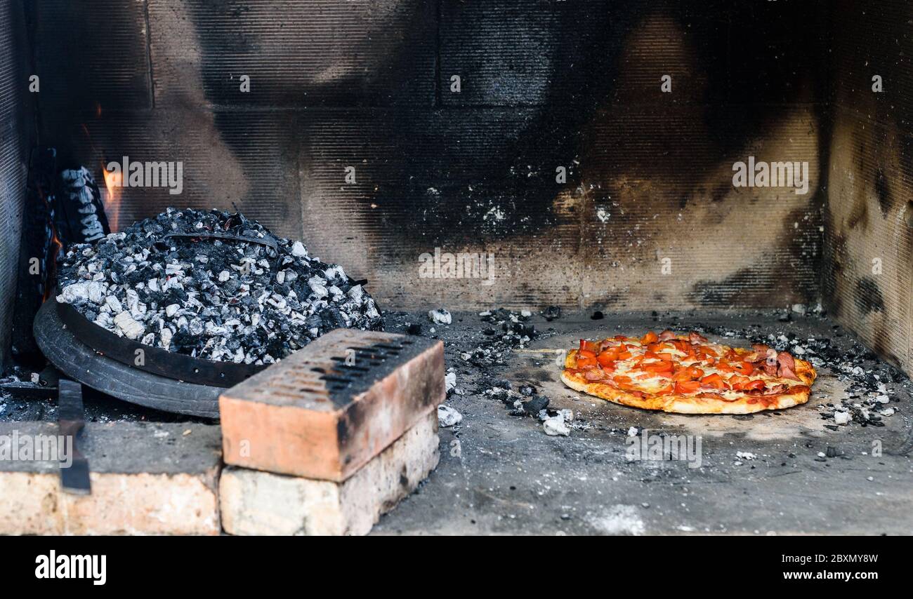 Making of homemade Italian pizza in fireplace brick oven. Making of traditional pizza in stone brick fireplace with fire wood and coals and a metall l Stock Photo