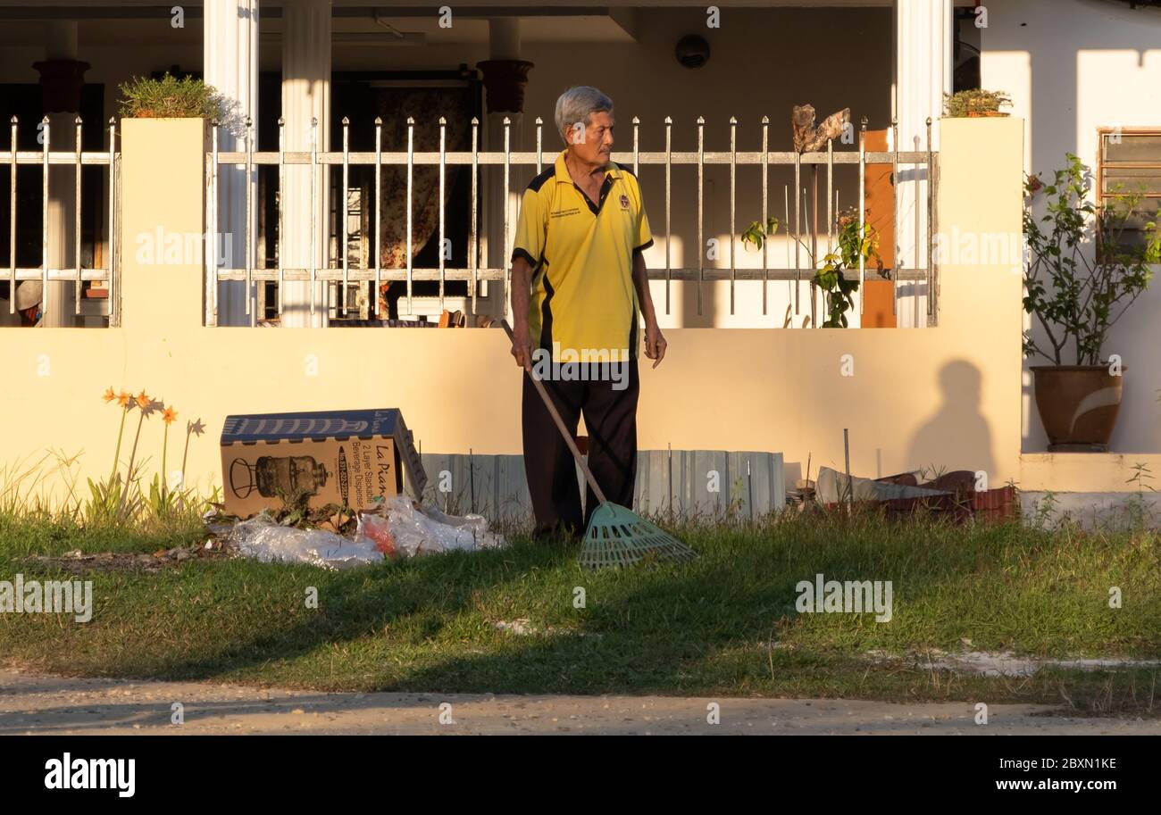 An elderly Malay man cleaning his garden in a rural village, Kuala