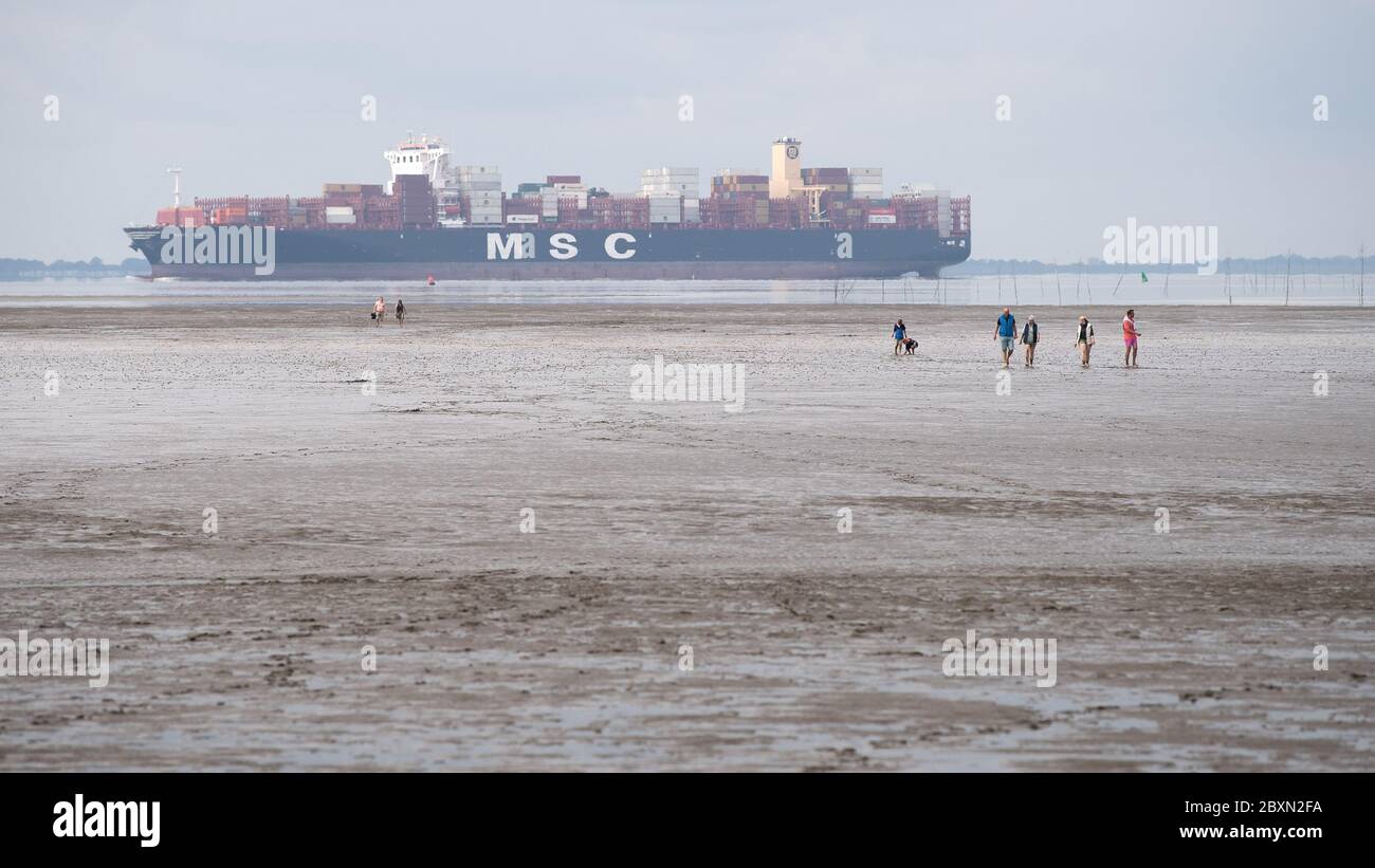 Wremen, Germany. 08th June, 2020. At low tide, walkers walk through the  mudflats on the North Sea beach Wremen. A container ship is sailing in the  background. The European Environment Agency EEA