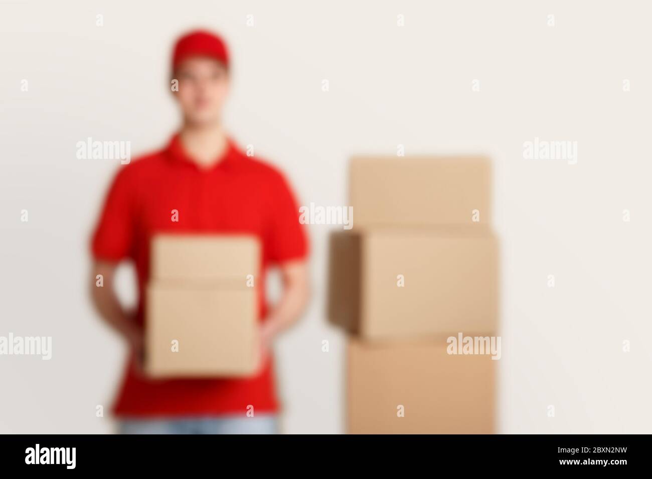 Blurry photo of courier in red uniform, holds parcels, near stack of boxes Stock Photo