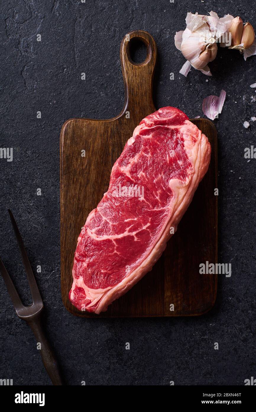 Top view Black Angus prime beef striploin steak on cutting board concrete background. Flat lay cooking ingredient Stock Photo