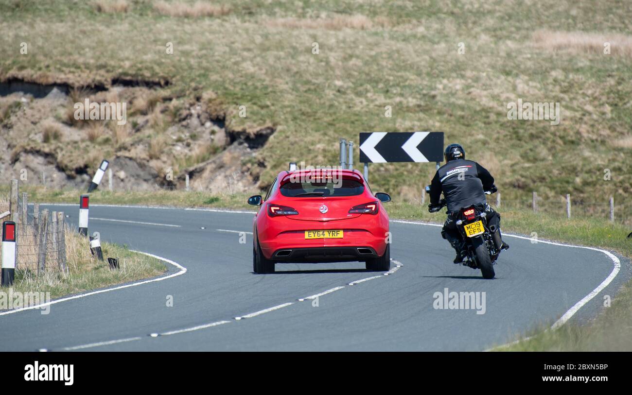 Motorcyclist overtaking a car on a dangerous corner on the B6255 Ingleton to Hawes road, where there are regular accidents. North Yorkshire, UK. Stock Photo