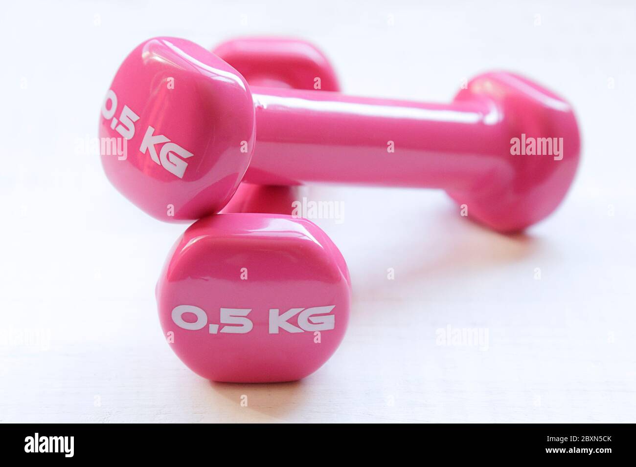 Pink dumbbells for fitness weighing 0.5 kg over a white wooden table Stock Photo