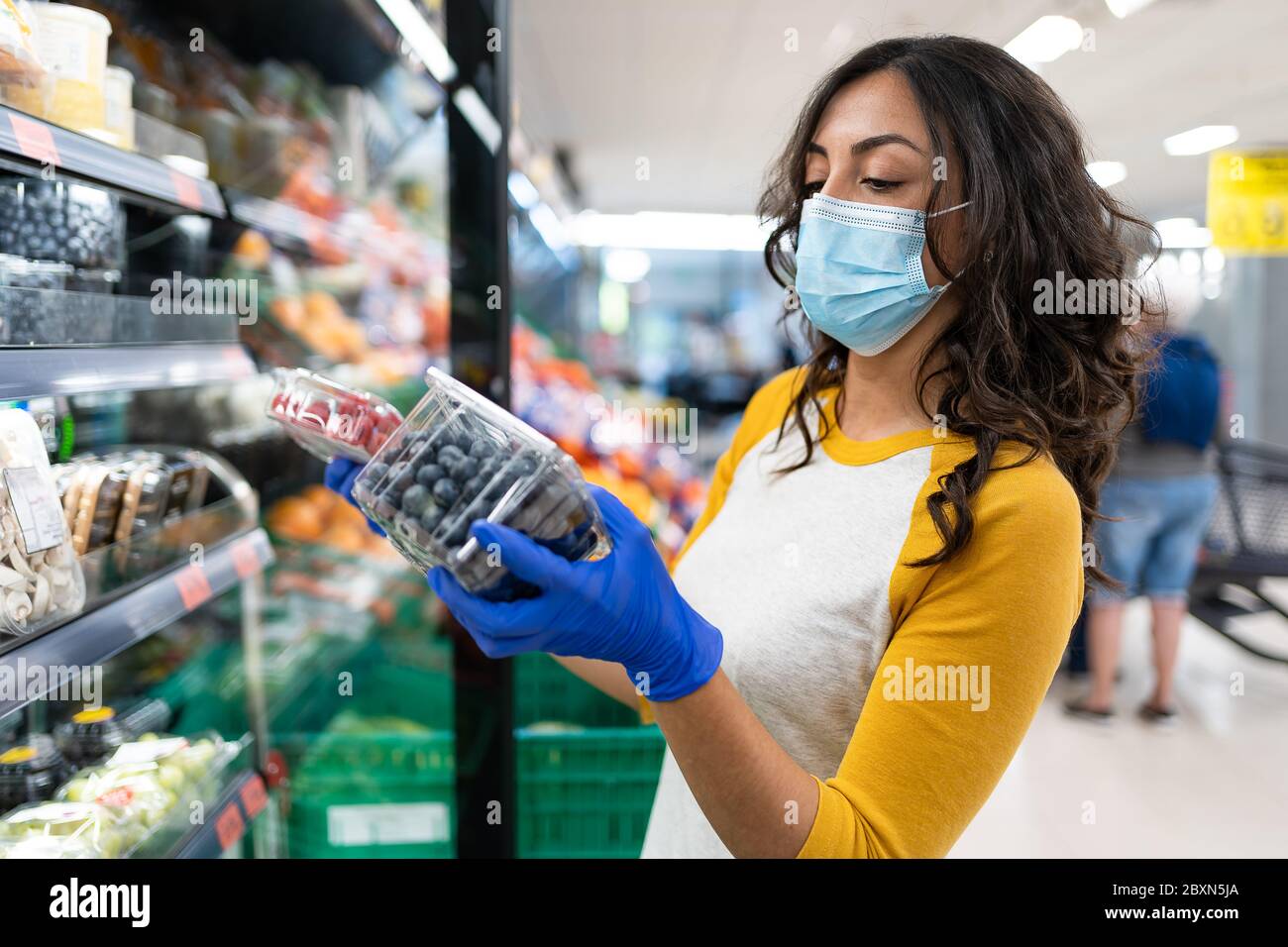 Woman buying two packs of red fruits at the supermarket in the fruit and vegetable section, protected by a mask and disposable gloves Stock Photo
