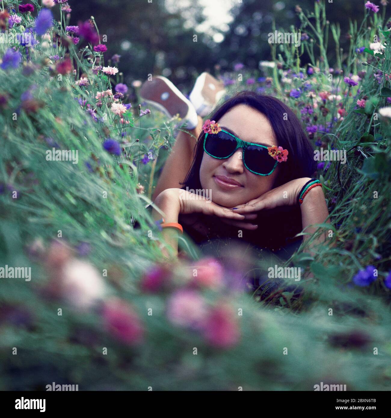 Young beautiful girl in sunglasses laying on the corn flowers field. Outdoor portrait, summer fun concept. Lifestyle photography. Stock Photo
