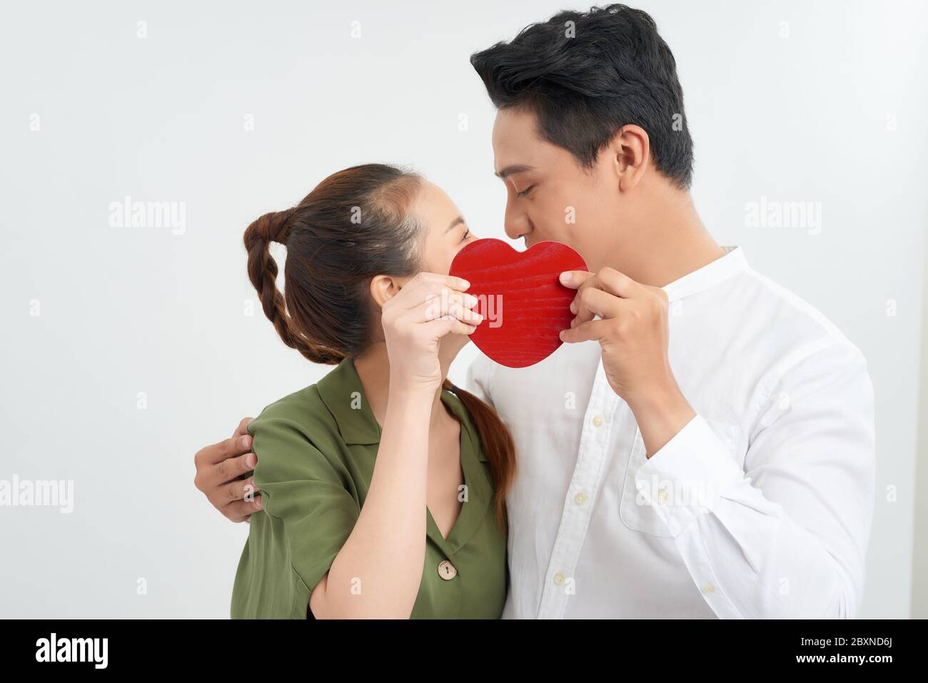Attractive young couple kissing behind large heart on white background