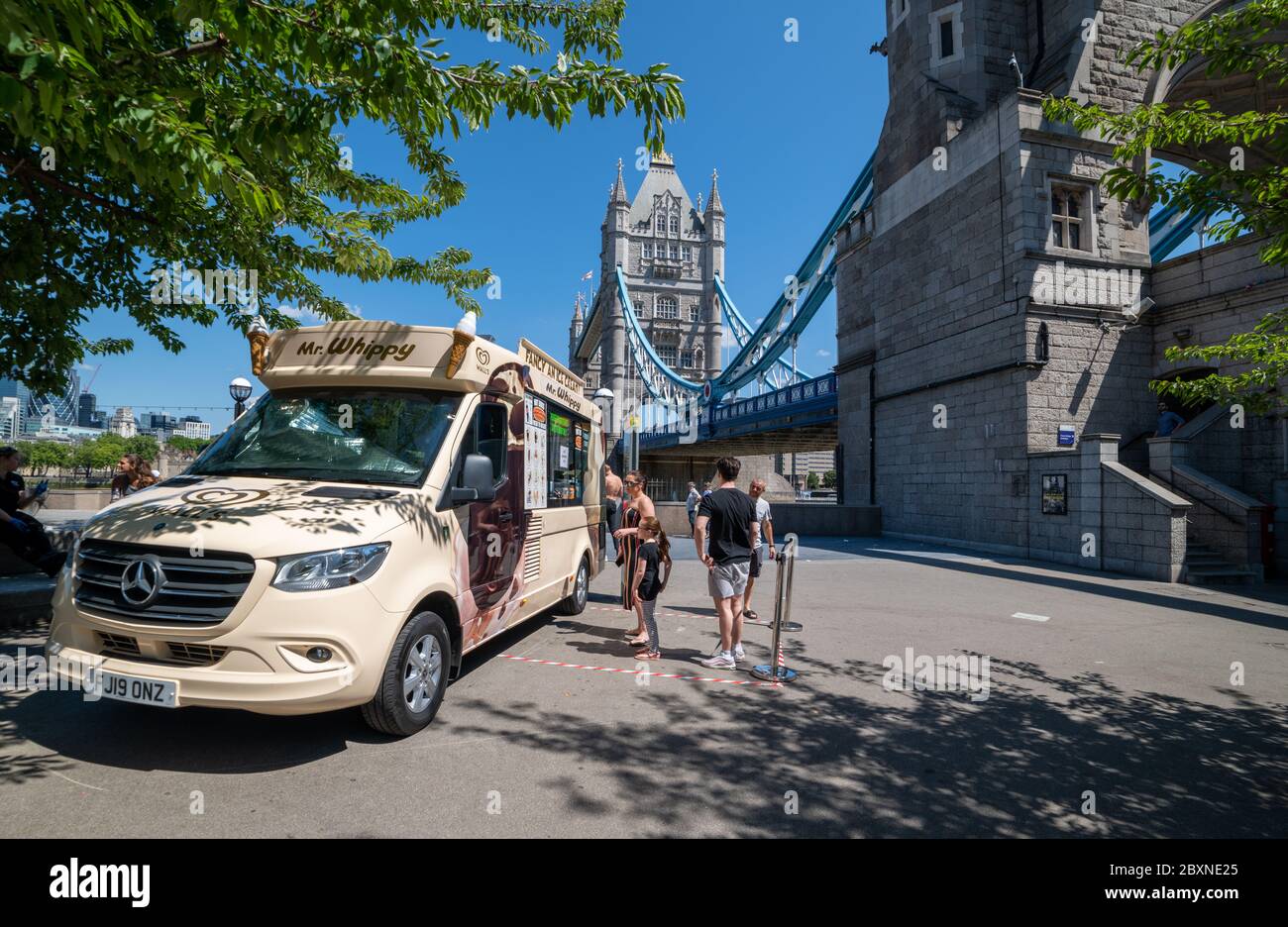 People buying drinks and ice cream from a ice cream seller with his van parked by Tower Bridge. Stock Photo