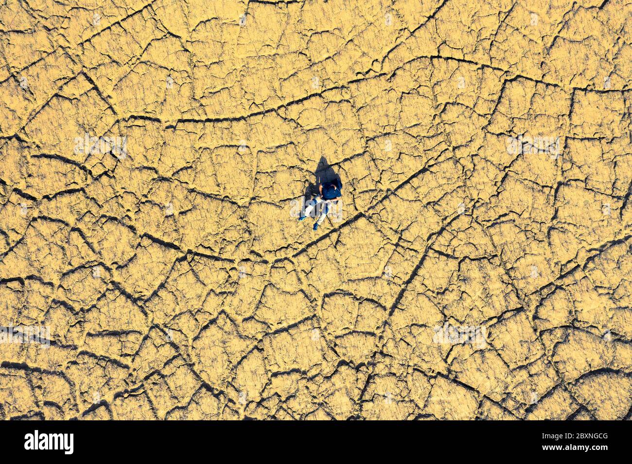 Man seated in a land cracked by drought. Stock Photo
