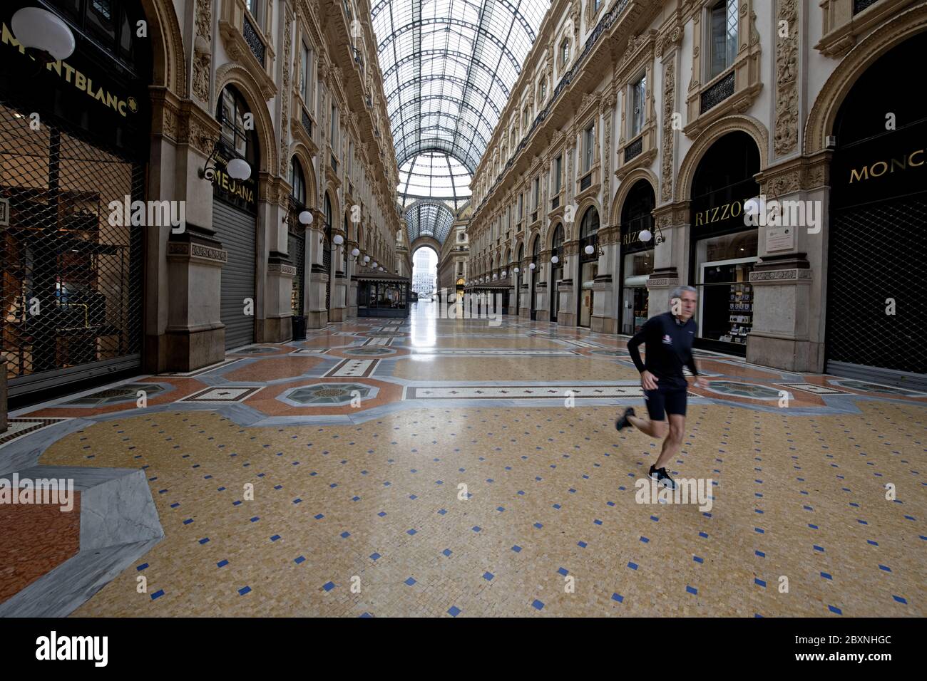 A man jogging in the emptiness of Galleria Vittorio Emanuele with shops closed during the lockdown caused by the Covid-19 in Milan, Italy. Stock Photo
