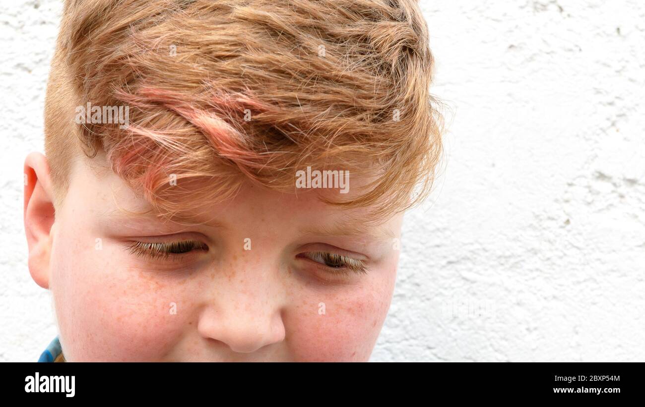 Plump red-haired boy is smiling. A boy in a plaid shirt stands on a wall background and smiles. Stock Photo