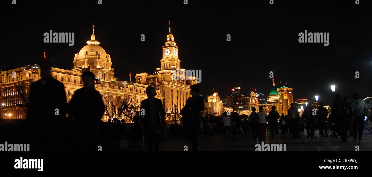 People on the Bund in Shanghai, China at night against a backdrop of illuminated buildings with the HSBC Building (left) and Custom House (center). Stock Photo