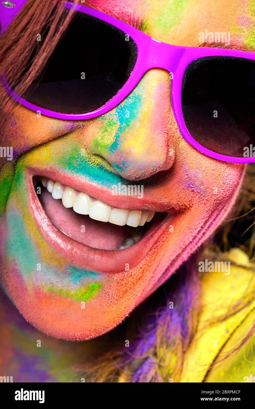 Happy young woman in fashionable purple sunglasses with a big smile and face covered in rainbow colorful powder having fun on the Hindu festival of Ho Stock Photo