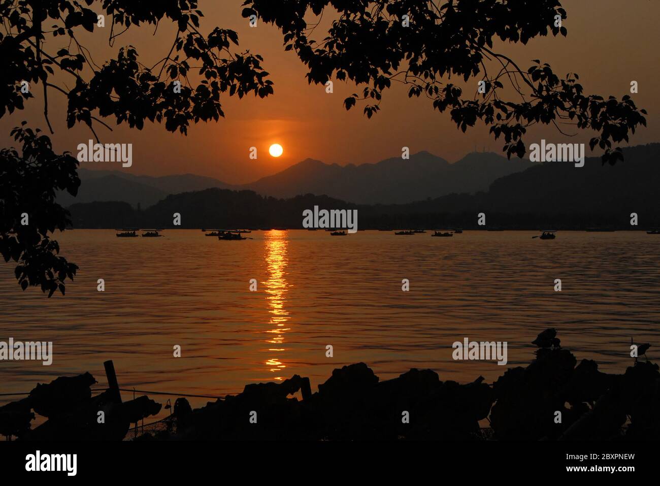 West Lake (Xi Hu) sunset in Hangzhou, Zhejiang Province, China. View of West Lake in Hangzhou at sunset with an orange light across the lake. Stock Photo