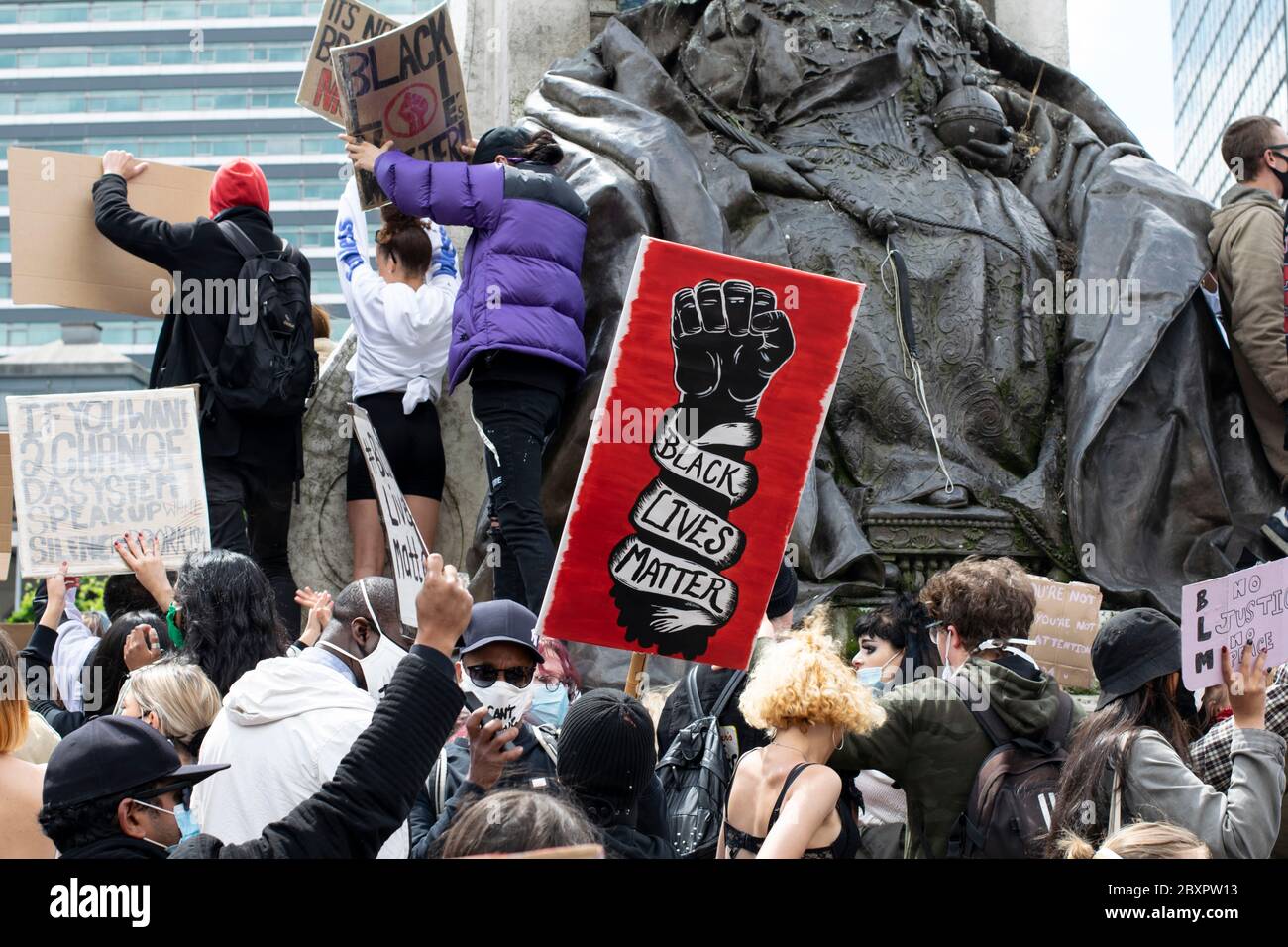 Black Lives Matter Protest, Manchester UK. Protesters on the plinth of Queen Victoria statue with red placard and black fist symbol Stock Photo