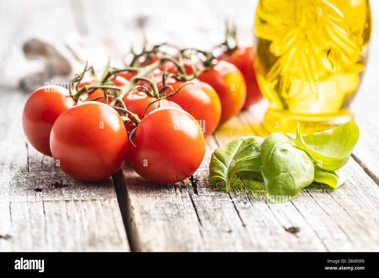 Red cherry tomatoes and basil leaves on wooden table. Stock Photo