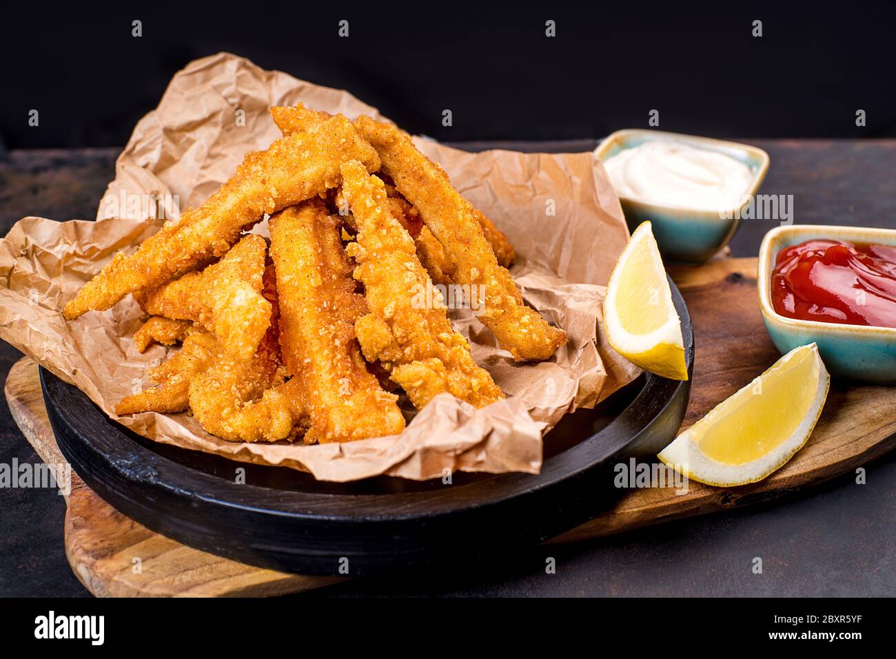 Fried chicken dippers in black bucket with sauce on black background