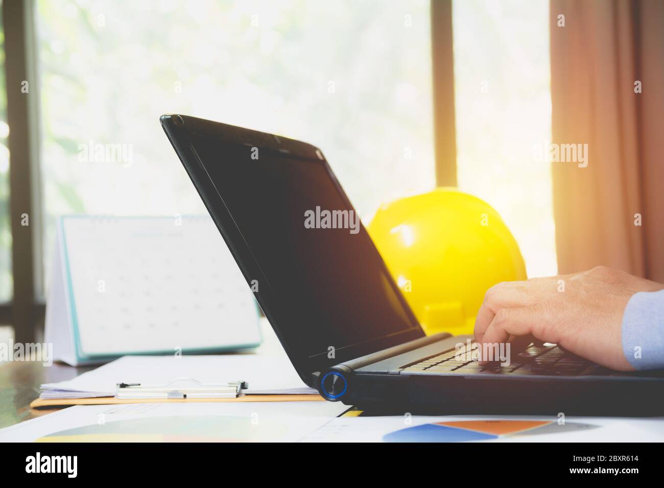 Architect engineer using laptop for working with yellow helmet on desk. Stock Photo