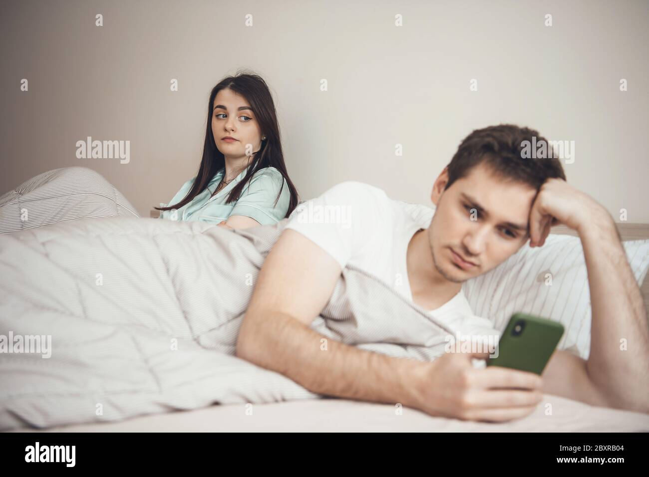 Jealous caucasian woman looking at his boyfriend in the bedroom chatting on mobile with somebody Stock Photo