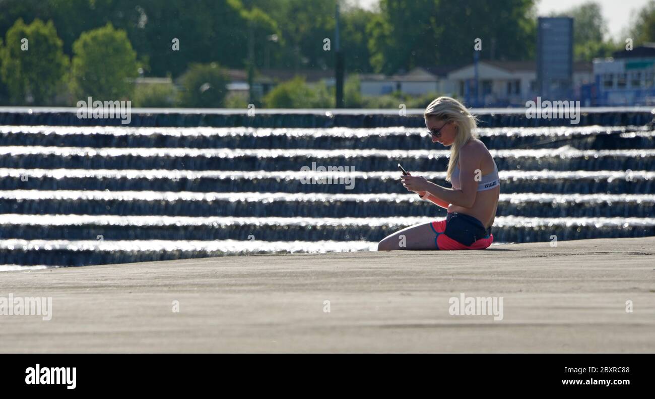 Young lady, sitting in the sun, looking at her phone, by the river Trent. Stock Photo