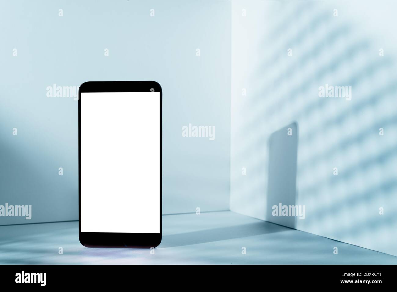 Minimalist modern smartphone mockup for presentation, in perspective in front of the corner angle of the wall, with overlapping shadows and blue gradi Stock Photo