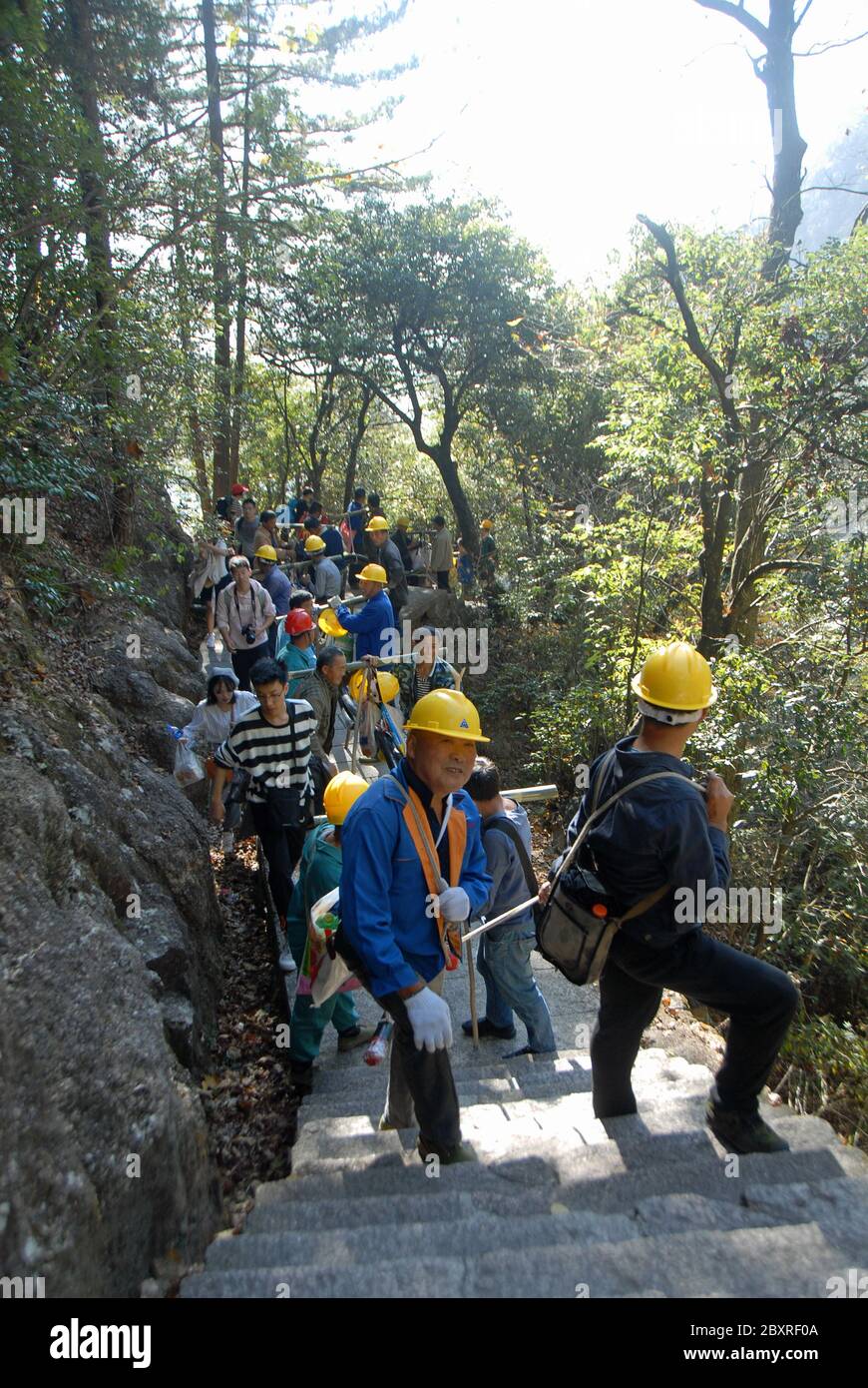 Huangshan Mountain in Anhui Province, China. Workers climbing the eastern steps of Huangshan hauling a very long pipe. Stock Photo