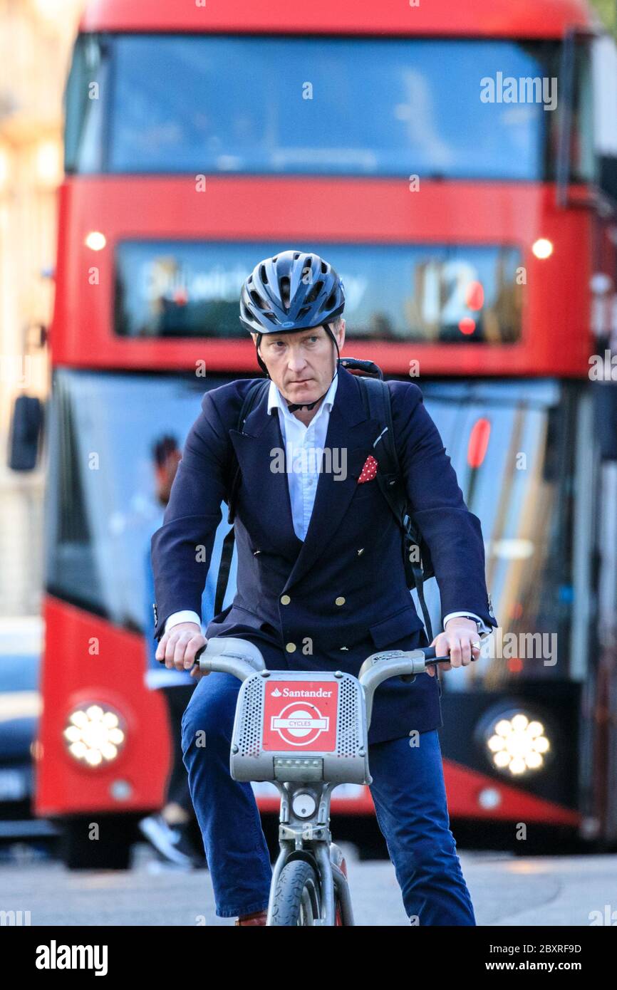 Suited male city cyclist on hire bike ahead of red bus in Westminster, Loondon, UK Stock Photo