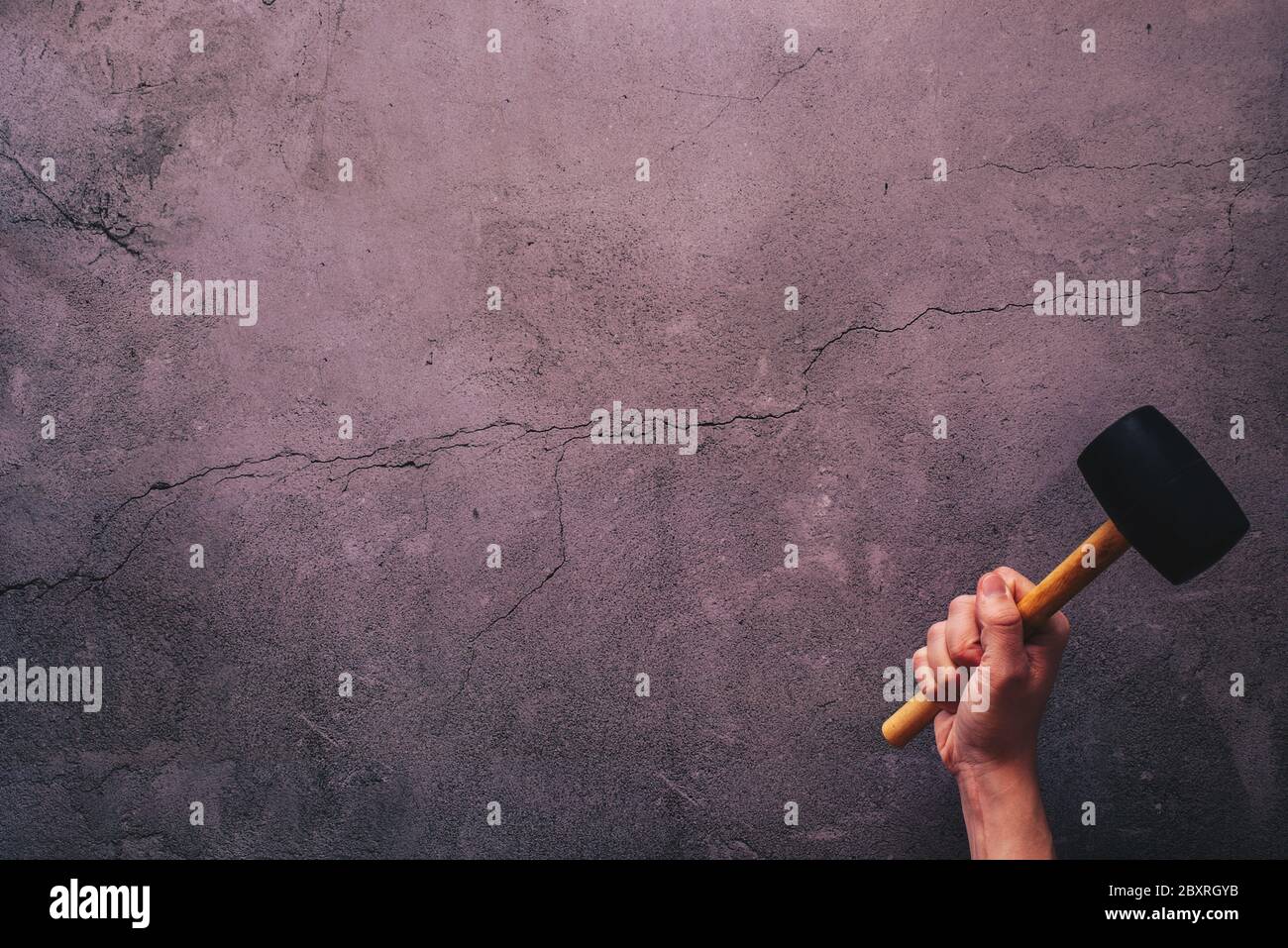 Hand holding a hammer hitting a cracked concrete background with plenty