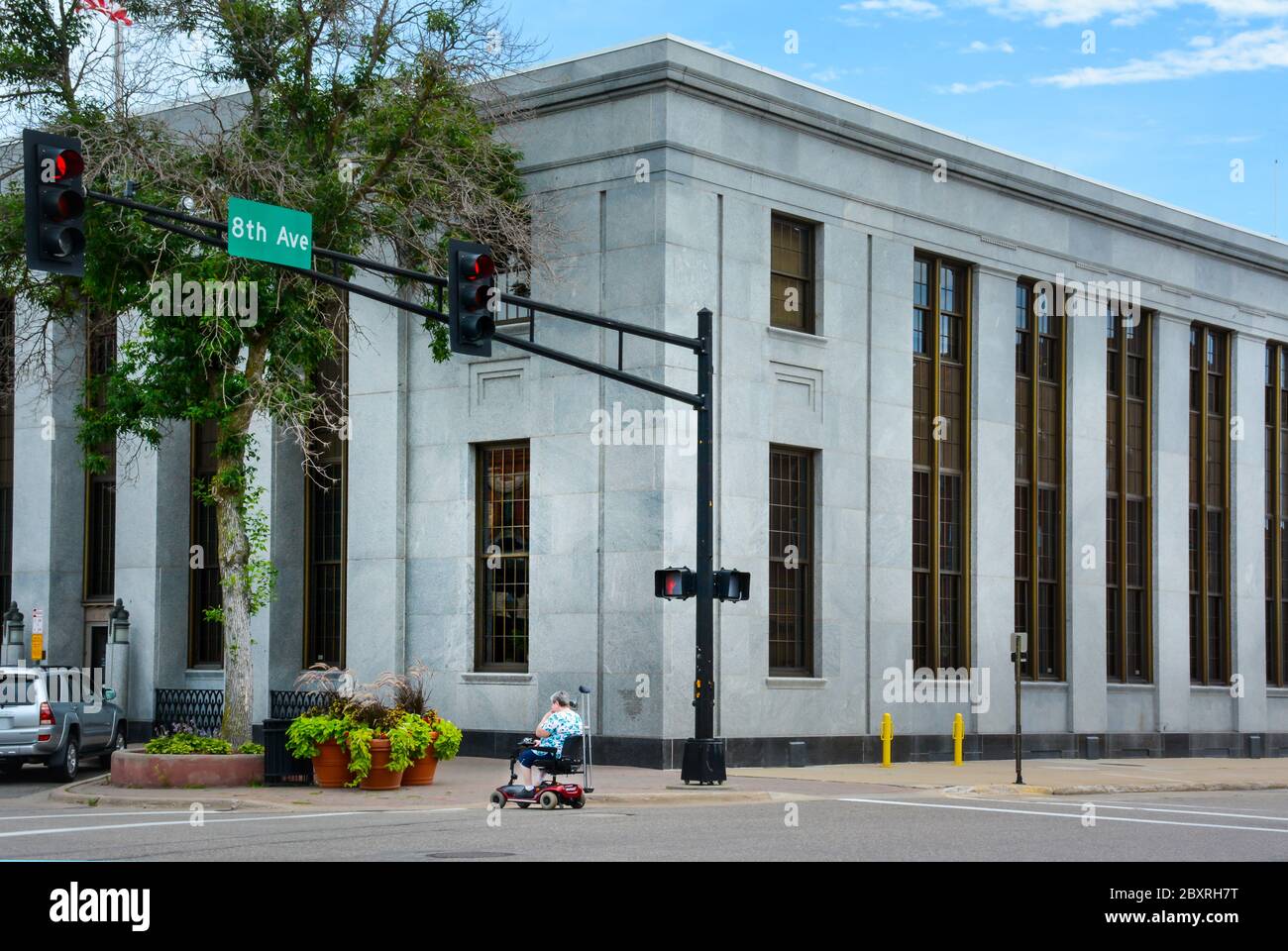 A senior citizen in a mobility scooter crosses 8th Avenue in front of the historic, former USPO building in downtown St. Cloud, MN, USA Stock Photo