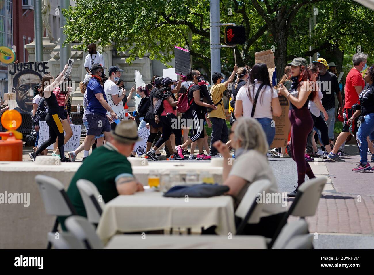A couple eats at the outdoor seating of a restaurant as hundreds of protesters march around them June 7, 2020, during a Black Lives Matter protest. Stock Photo